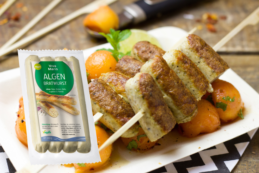 Viva Maris ALGEN Bratwurst in der Packung neben einem Spieß mit gebratener Algen Bratwurst